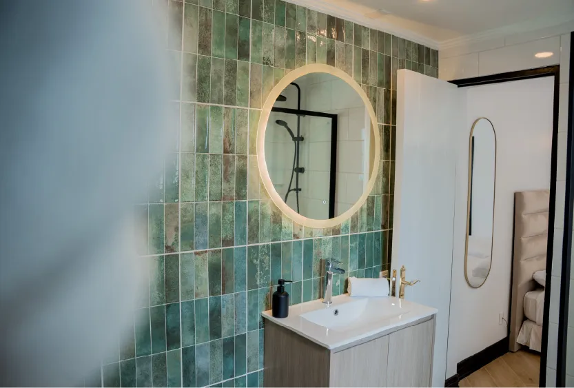 Baño con muro de cerámica verde y espejo redondo iluminado